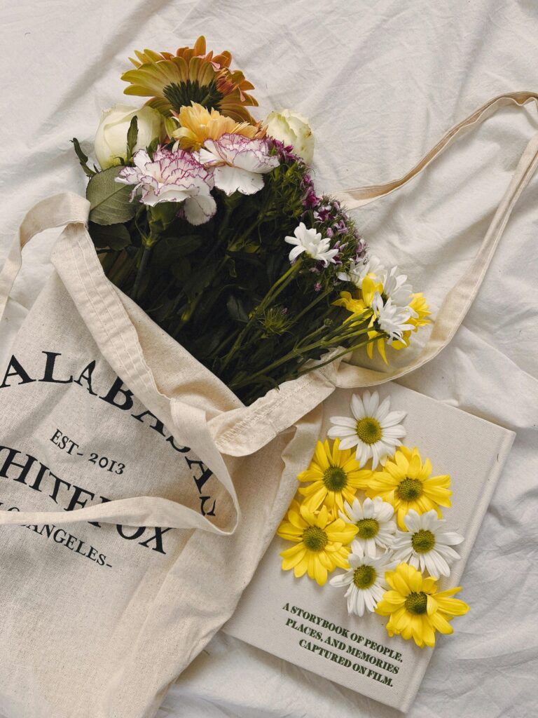 pexels-photo-30908216-30908216 Tote bag filled with colorful flowers next to an artistic floral book.