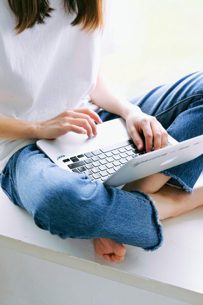 pexels-photo-3987114-3987114 Woman sitting cross-legged in casual jeans working on a laptop indoors.
