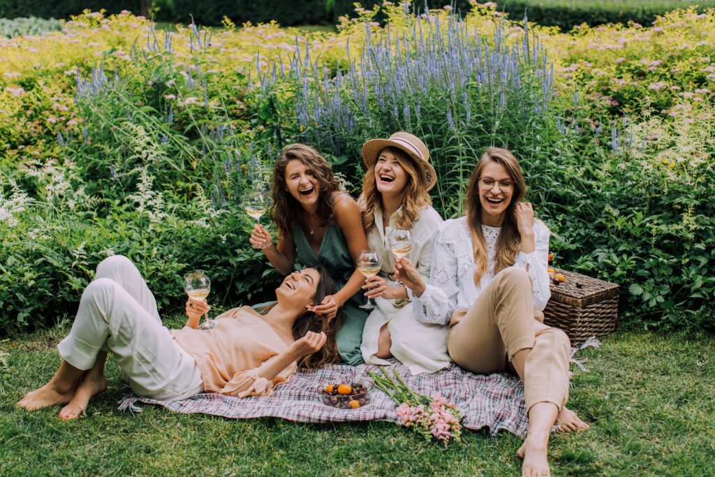 pexels-photo-4833957-4833957 Four women enjoying a picnic, laughter, and wine in a vibrant summer garden.