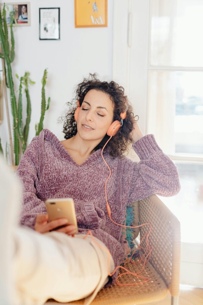 pexels-photo-6633273-6633273 Woman sitting indoors enjoying music with headphones and smartphone.